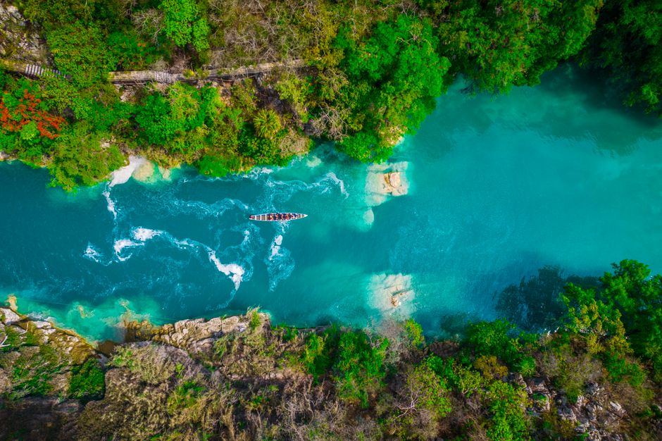 Vista aérea de un río de aguas turquesa entre vegetación en la Huasteca potosina, con una lancha diminuta y sin rostros visibles