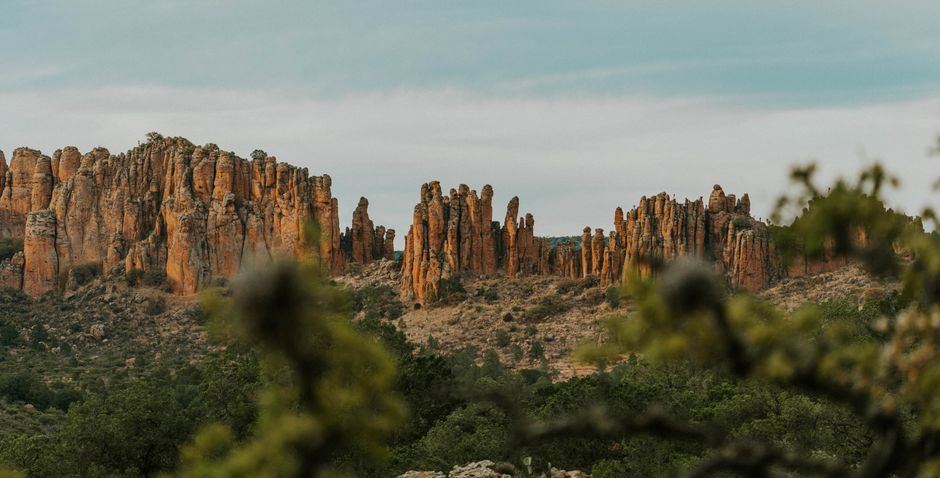 Columnas de roca anaranjada entre vegetación verde bajo un cielo nublado, sin personas
