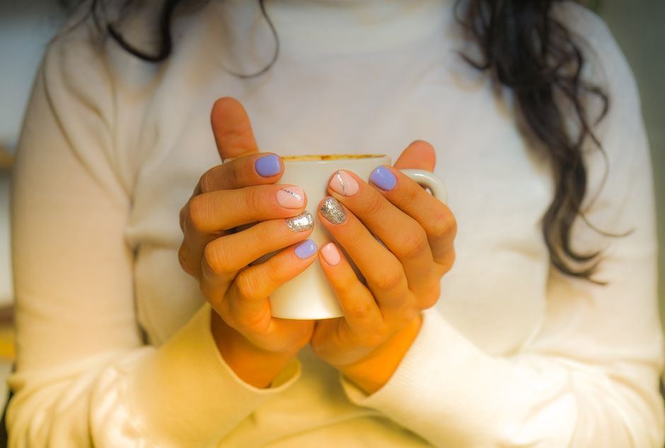 Dos manos sostienen con calma una taza blanca, con un suéter claro y luz cálida, sin rostro visible