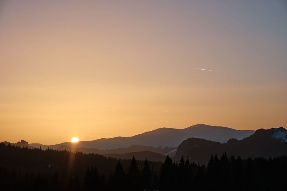 Amanecer cálido detrás de montañas y bosque, con el sol asomando en el horizonte