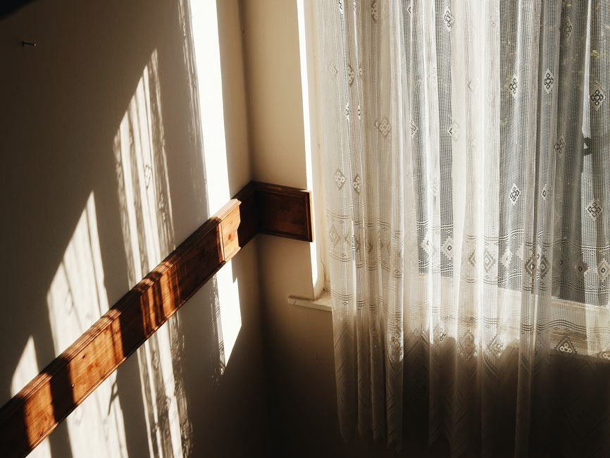 Cortina de encaje blanco junto a una ventana, con luz cálida de la mañana sobre la pared