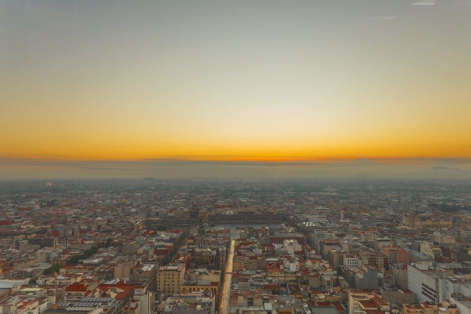 Vista aérea del centro de la Ciudad de México al amanecer, con el cielo anaranjado sobre los edificios