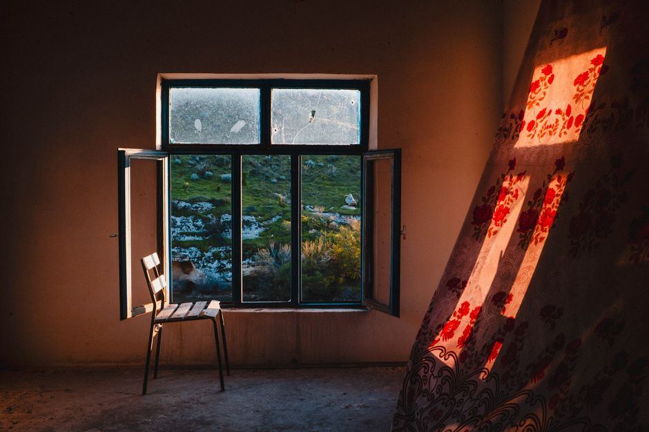 Habitación con una ventana abierta, una silla de madera vacía y luz cálida de la tarde, sin personas