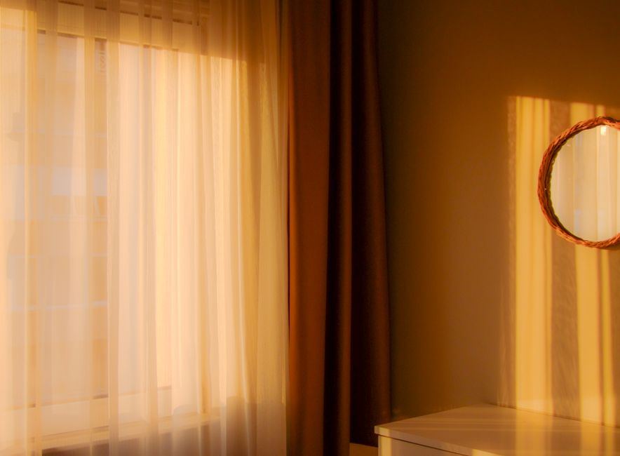 Luz cálida de la mañana entrando por una cortina translúcida junto a un espejo redondo, sin personas
