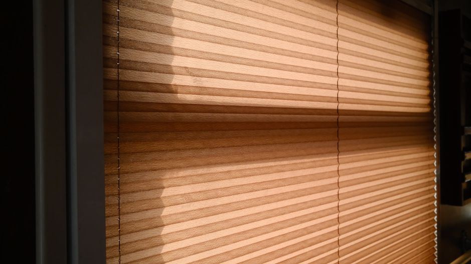 Persiana plisada de tono cálido con sombras de luz de tarde, sin personas