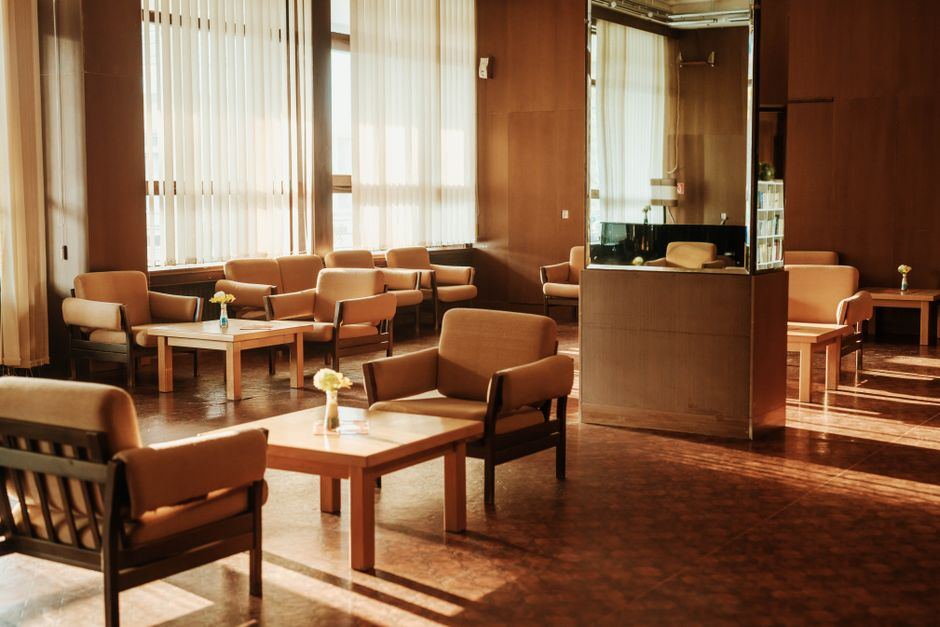 Sala de espera vacía con sillones y mesas de madera, iluminada por la luz cálida de las ventanas