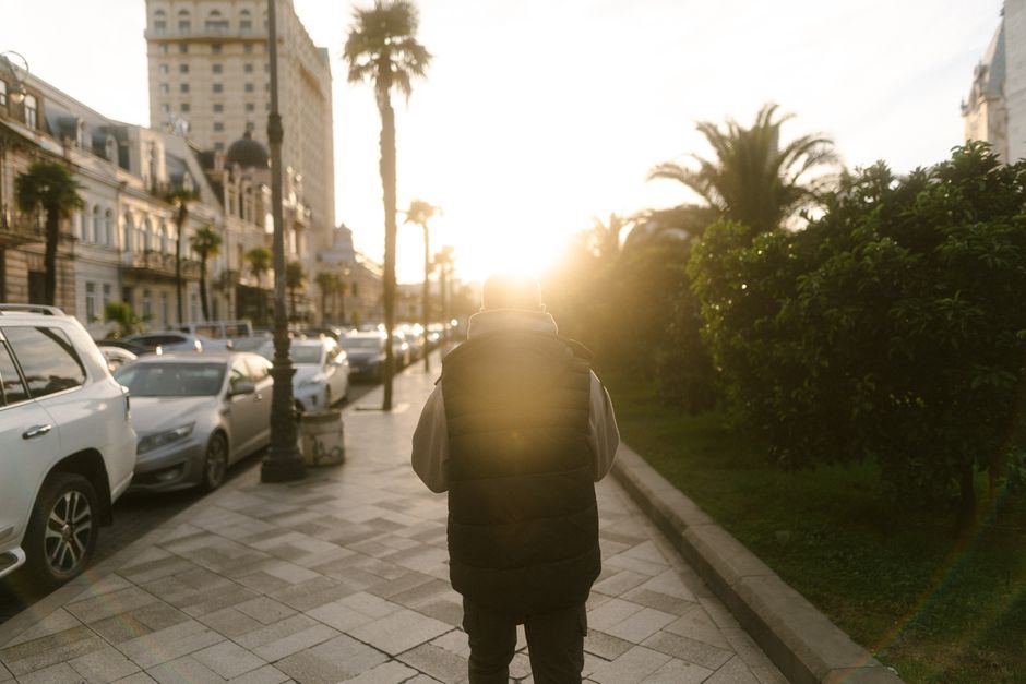 Persona vista de espaldas caminando por una banqueta al atardecer, con palmeras y luz dorada al fondo