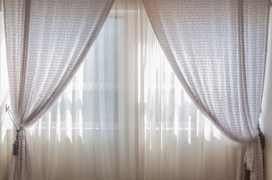 Cortinas claras recogidas a los lados de una ventana por la que entra luz natural, sin personas