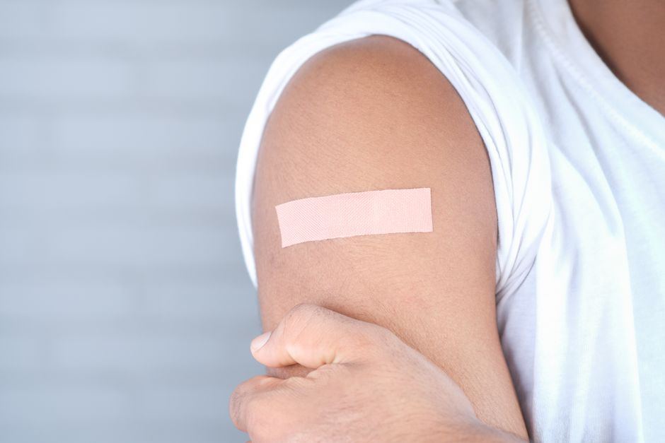 Hombro de una persona con un parche adhesivo después de una vacuna, sin rostro visible